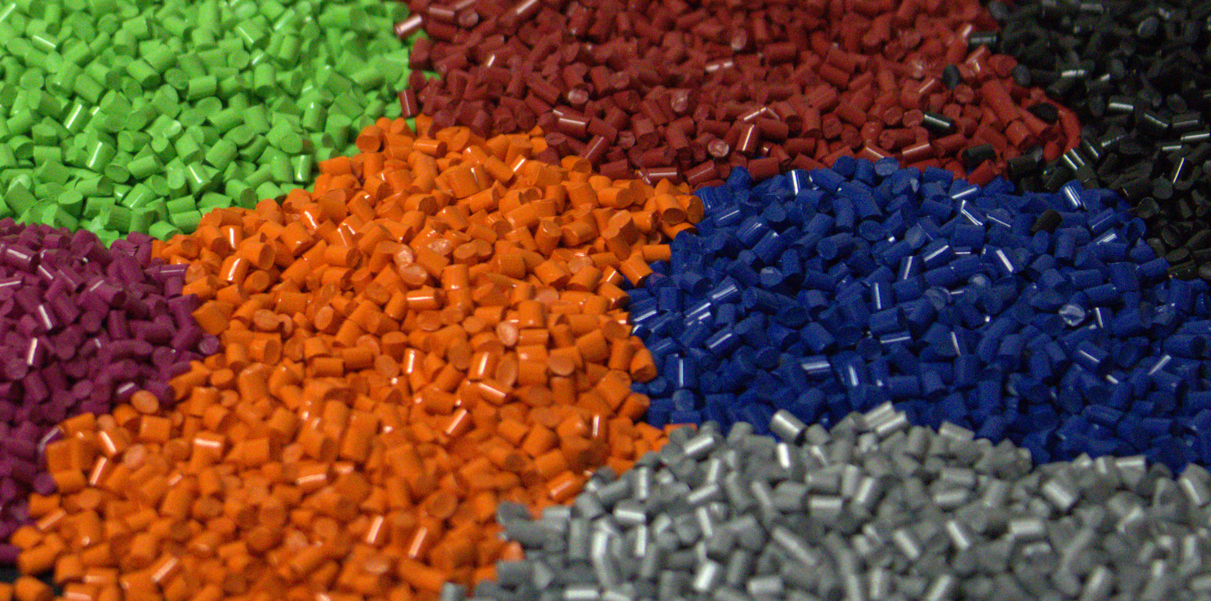Colorful plastic pellets in various hues including green, red, orange, blue, purple, and gray.